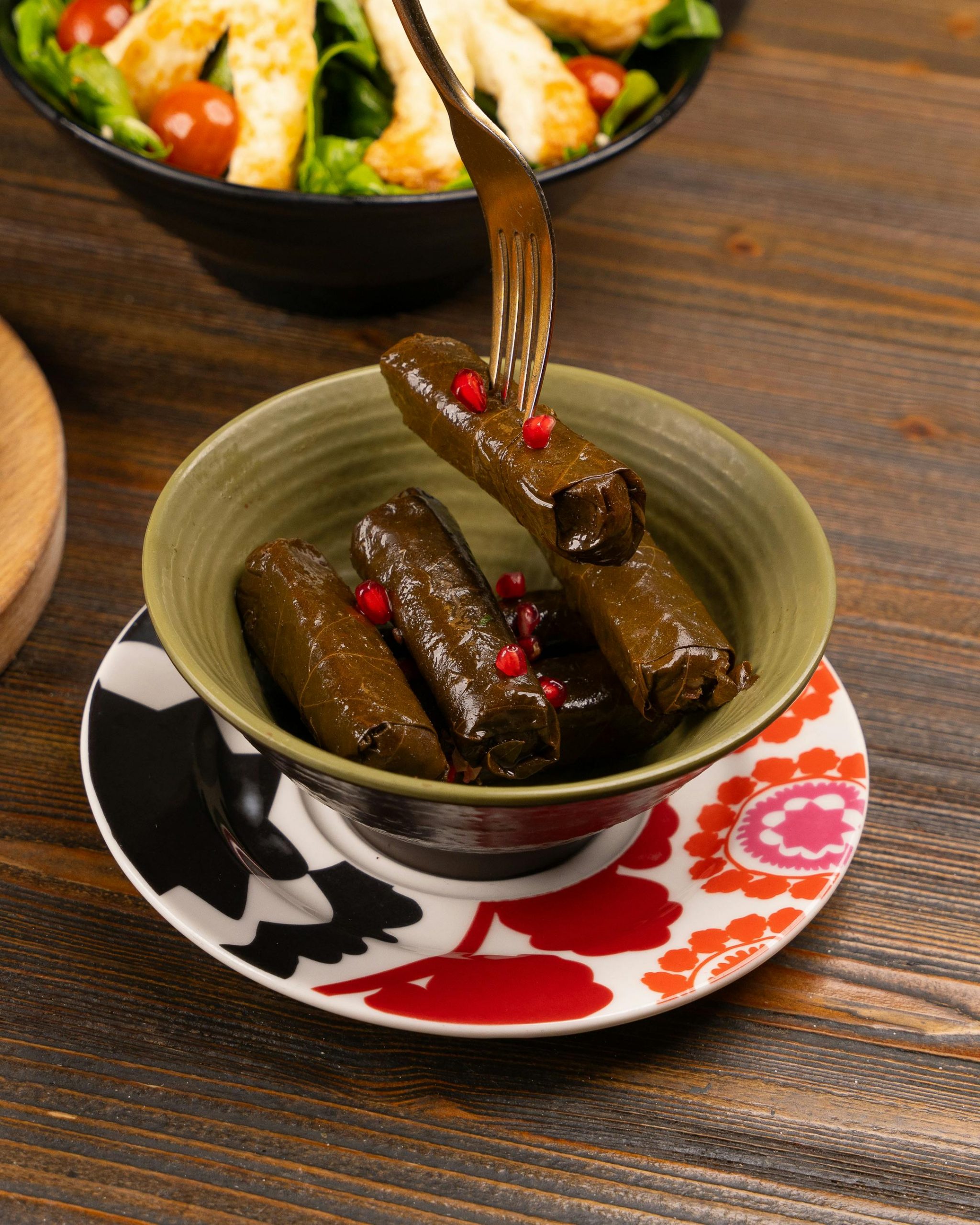 Mediterranean stuffed grape leaves with pomegranate seeds served on a decorative plate.