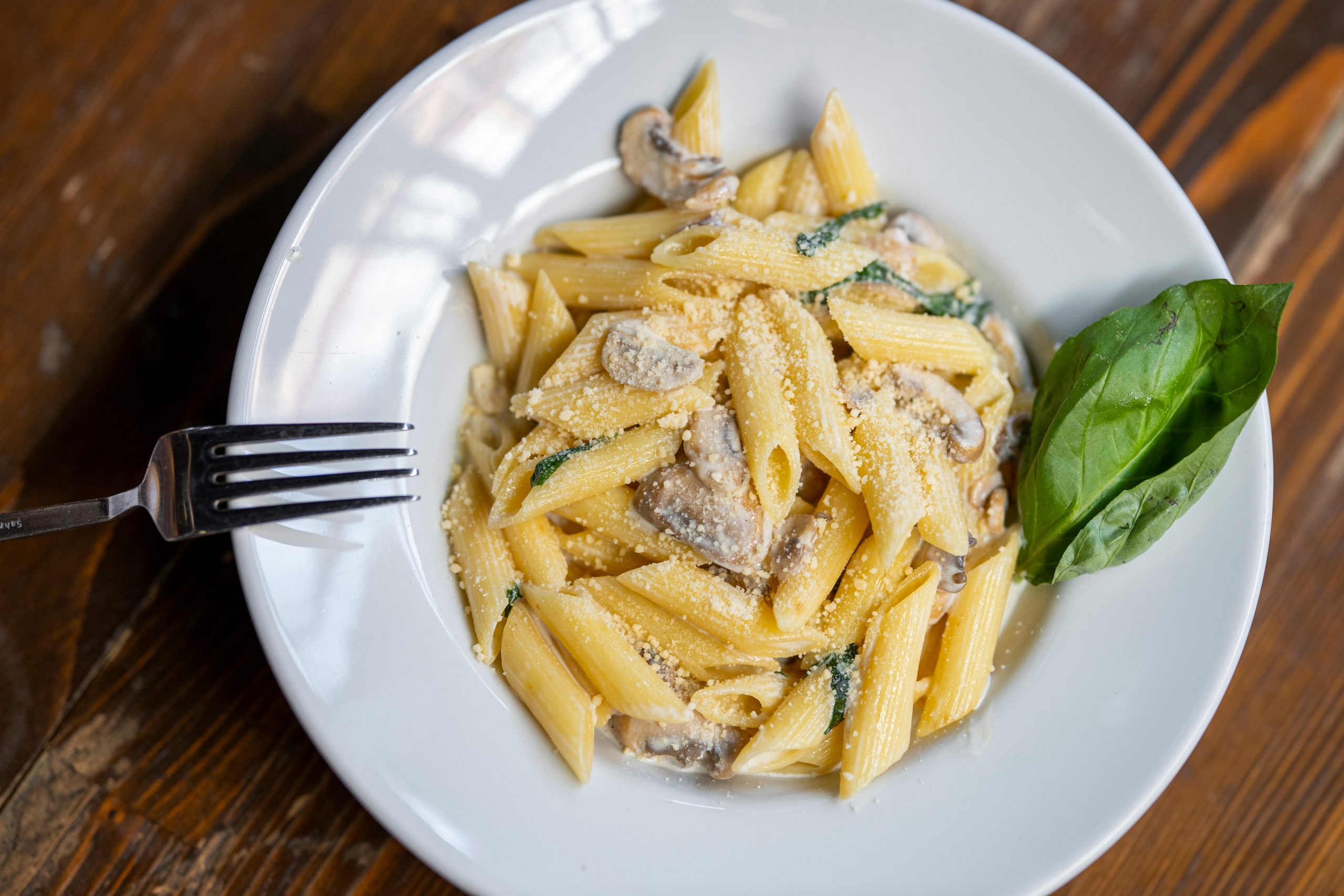 Tasty penne pasta with mushrooms in creamy sauce garnished with basil on a wooden table.